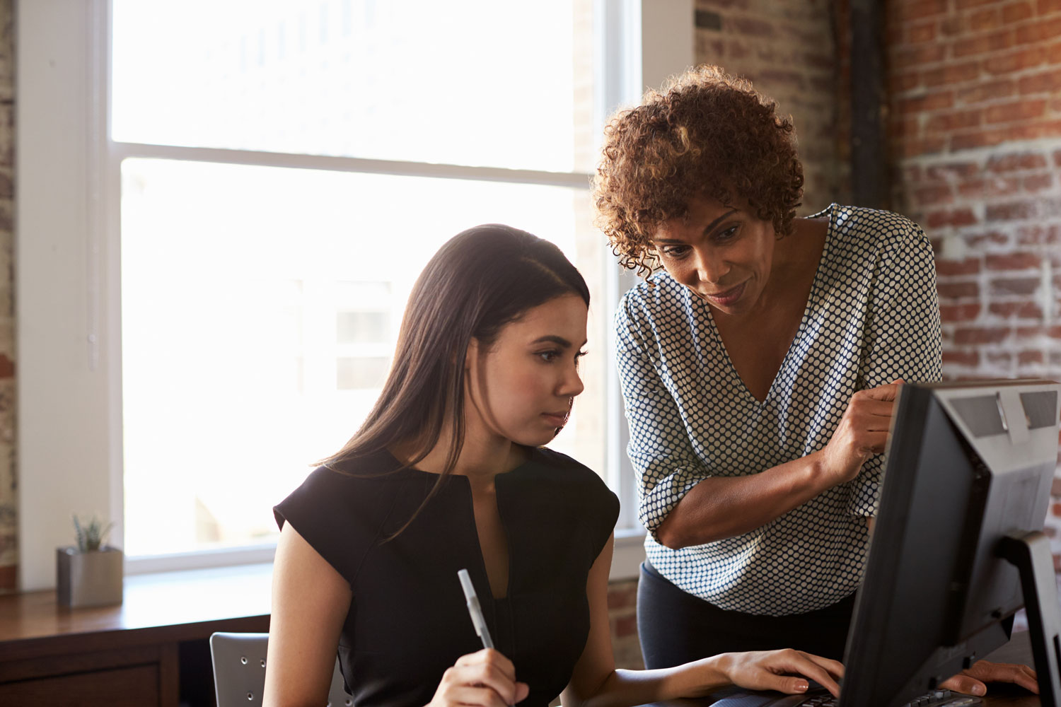 Woman looking over shoulder of younger woman with laptop