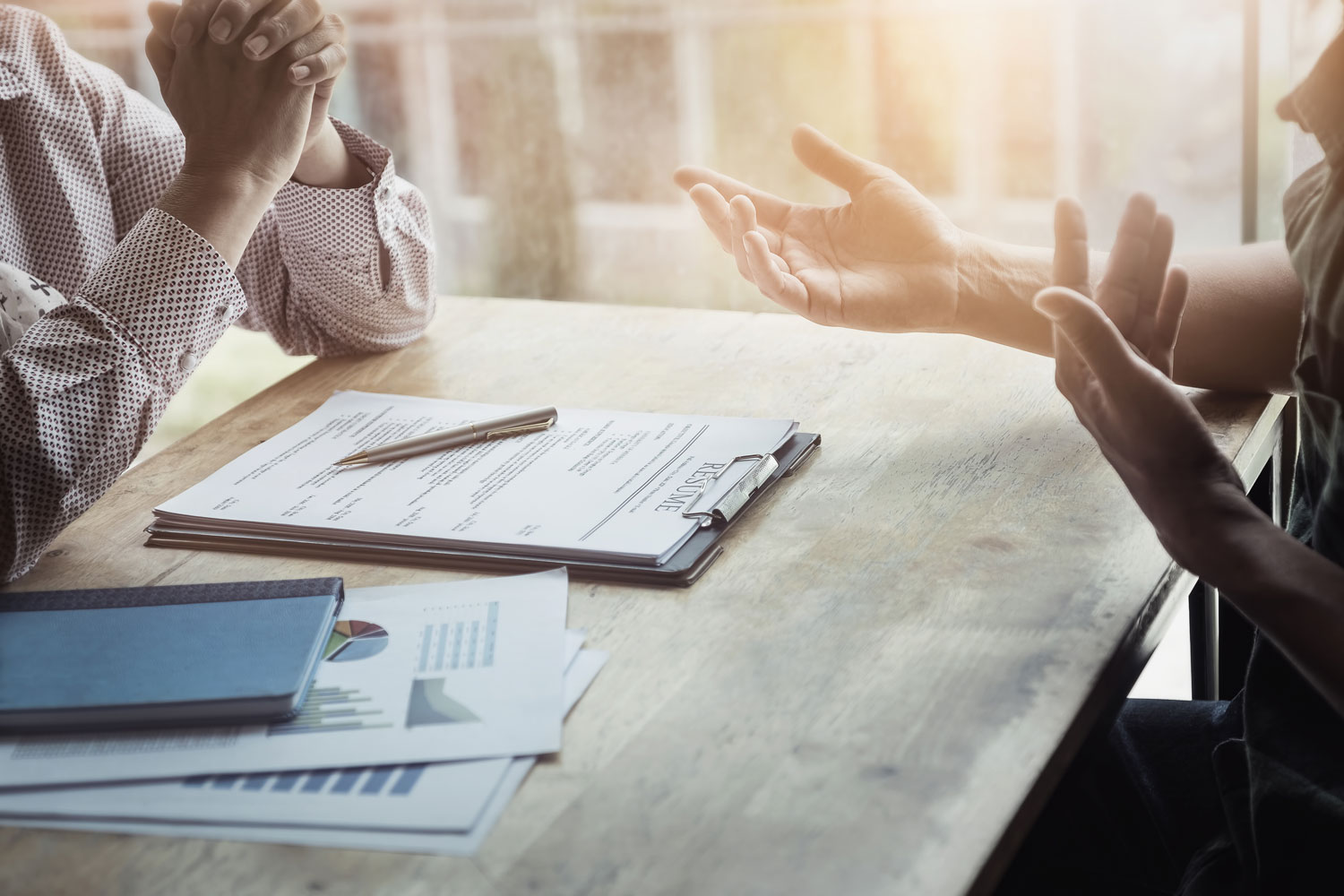 two sets of hands gesturing above a resume on clipboard