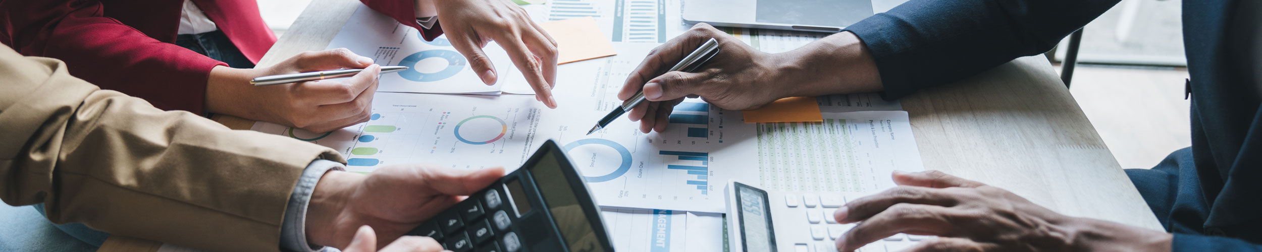 close-up of multiple hands with calculators and pens at conference table