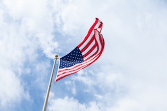 American flag waving in the wind with clouds and blue sky behind it